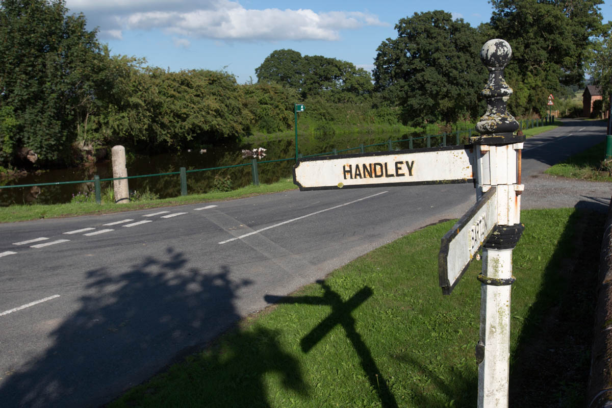 Picturesque summer view of a rustic village direction sign in the Cheshire village of Coddington, with the village pond in the background.